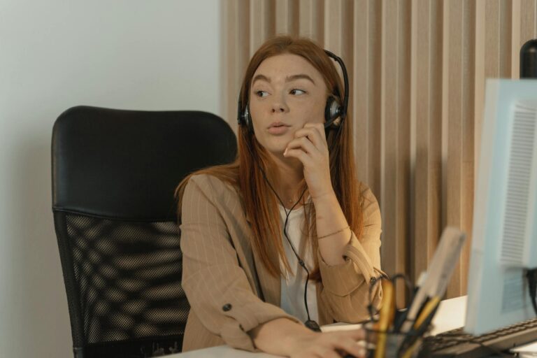 Young woman seated at a desk talking with a headset in a modern office environment.